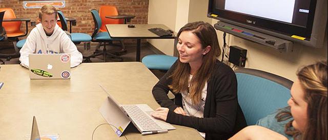 Three students sitting in classroom with laptops